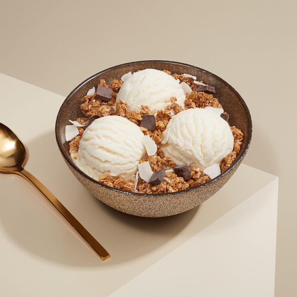 A bowl of ice cream topped with organic dark chocolate coconut granola, featuring scoops of vanilla ice cream and chocolate pieces.