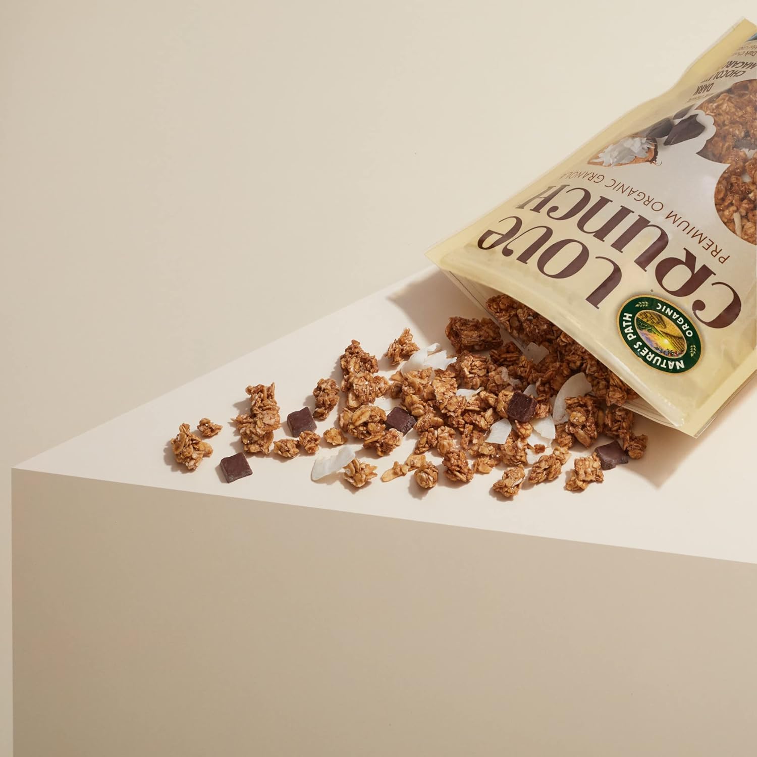 organic dark chocolate coconut granola spilling from an opened bag on a minimalistic surface