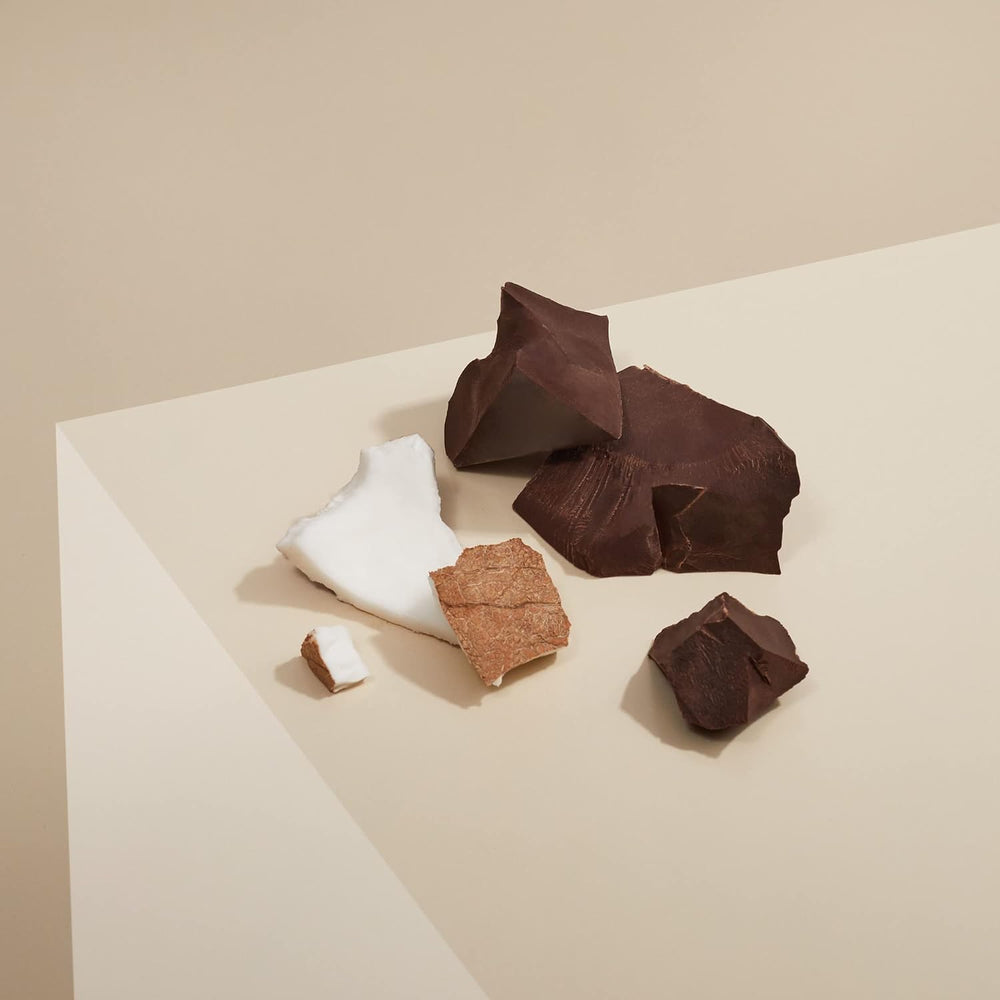 pieces of organic dark chocolate and coconut on a beige background, representing organic dark chocolate coconut granola.